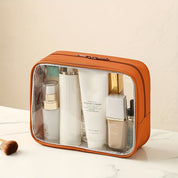 Borsa trasparente per cosmetici in pelle arancione, contenente flaconi di prodotti per la cura della pelle e trucco, su sfondo chiaro.
