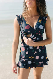Donna in spiaggia con tuta corta floreale, scollo a V, colori vivaci. Moda estiva, abbigliamento casual, look trendy per il mare.