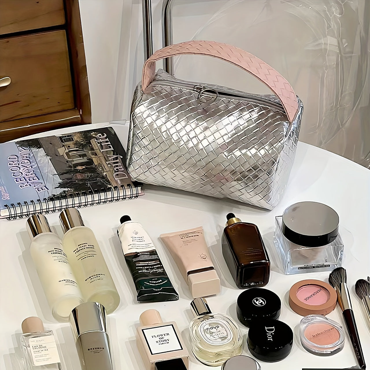 Borsa cosmetica intrecciata argento su tavolo con prodotti di bellezza: creme, profumi, trucco. Accessori moda e bellezza, stile elegante.