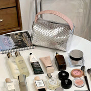 Borsa cosmetica intrecciata argento su tavolo con prodotti di bellezza: creme, profumi, trucco. Accessori moda e bellezza, stile elegante.