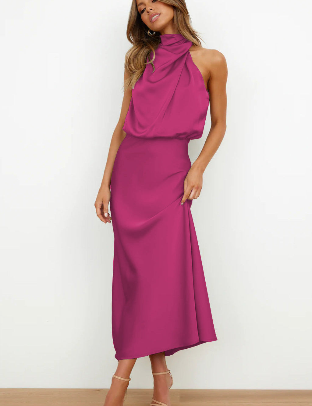 Abito lungo fucsia elegante, senza maniche, con collo alto drappeggiato. Perfetto per eventi formali. Modella in posa su sfondo bianco.