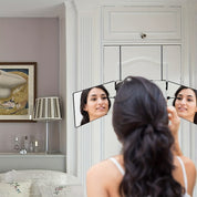 Donna che si guarda in uno specchio triplo pieghevole in camera da letto elegante, con lampada e quadro. Specchio trucco, arredamento moderno.