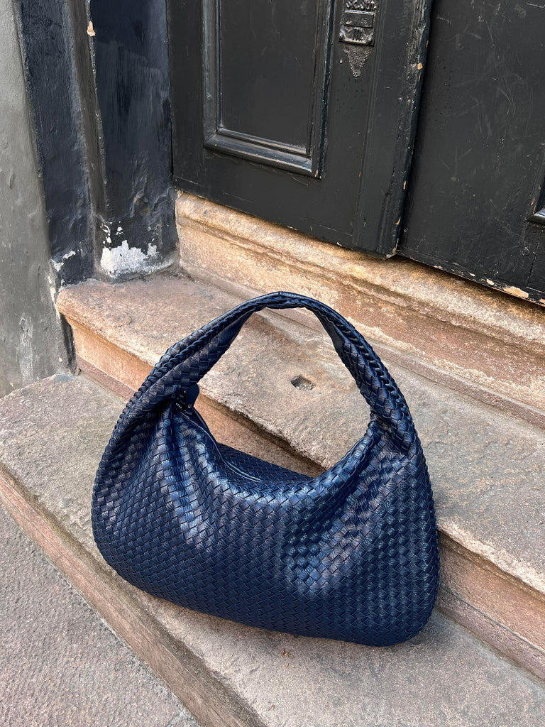 Borsa a spalla intrecciata blu scuro su gradino di pietra, design elegante e moderno, accessorio moda donna, perfetto per look casual e chic.