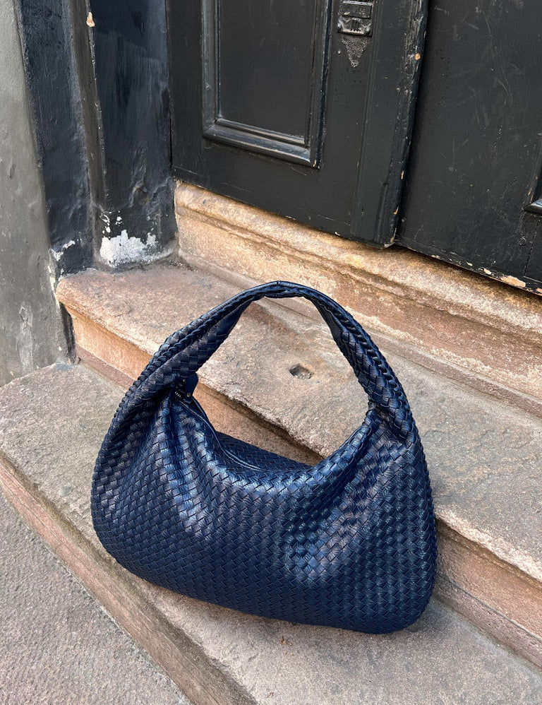 Borsa a spalla intrecciata blu scuro su gradini di pietra, design elegante e moderno, accessorio moda donna, perfetto per look casual e chic.