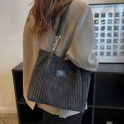 Donna con borsa a tracolla in velluto a coste grigio, giacca beige. Accessorio moda elegante, perfetto per look autunnali.