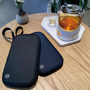 Borse termiche nere su tavolo in legno accanto a teiera in vetro con tè caldo e tazza. Accessori eleganti per mantenere bevande calde.
