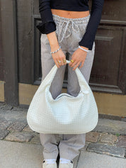 Donna con borsa a spalla bianca intrecciata, pantaloni a righe bianche e nere, top nero. Moda casual, accessori eleganti, street style.