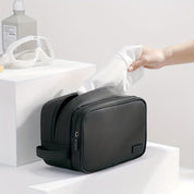 Borsa da toilette nera in pelle, elegante e spaziosa, con cerniera, ideale per viaggi. Mano che inserisce un asciugamano bianco. Accessori bagno moderni.