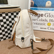 Zaino bianco in tessuto con cerniere e tasche multiple, su sfondo interno. Design moderno, ideale per scuola o viaggio. Accessorio moda unisex.