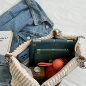 Borsa a tracolla in tessuto beige con tasche interne, contenente tablet, smartphone, bottiglia d'acqua e giacca di jeans. Accessori moda casual.