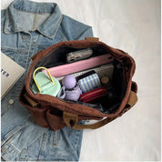 Borsa a tracolla marrone su giacca di jeans, contenente accessori vari come bottiglia d'acqua, astuccio, rossetto e smartphone. Accessori moda casual.