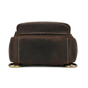 Zaino in pelle marrone scuro, design compatto, cuciture bianche, anelli metallici dorati, ideale per viaggi e uso quotidiano. Accessorio moda uomo.