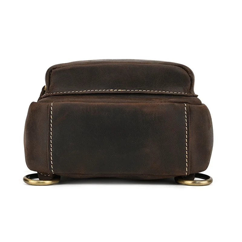 Zaino in pelle marrone scuro, design compatto, cuciture bianche, anelli metallici dorati, ideale per viaggi e uso quotidiano. Accessorio moda uomo.