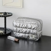 Borsa da toilette argentata su tavolo nero, design trapuntato, marchio "hello trip", accanto a vassoio con perle e rossetto. Accessorio da viaggio elegante.