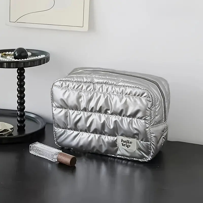 Borsa da toilette argentata su tavolo nero, design trapuntato, marchio "hello trip", accanto a vassoio con perle e rossetto. Accessorio da viaggio elegante.
