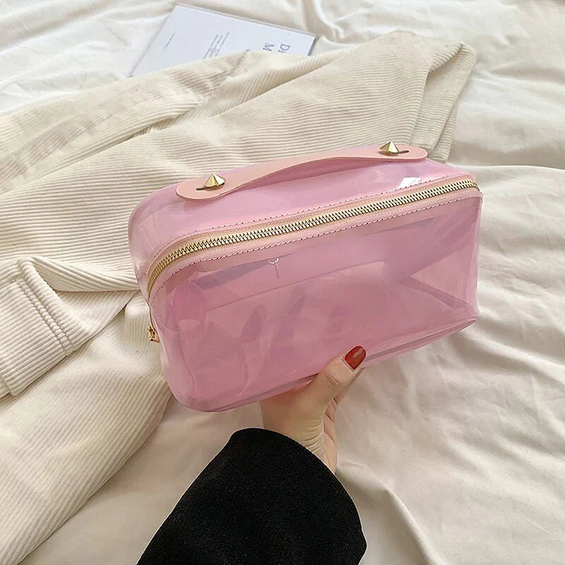 Astuccio trasparente rosa con cerniera dorata, design elegante, ideale per cosmetici e accessori da viaggio. Perfetto per organizzazione e stile.