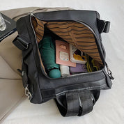 Zaino nero aperto su letto, mostra interno con oggetti personali: bottiglia verde, libro, astuccio rosa. Design moderno, ideale per viaggi e scuola.