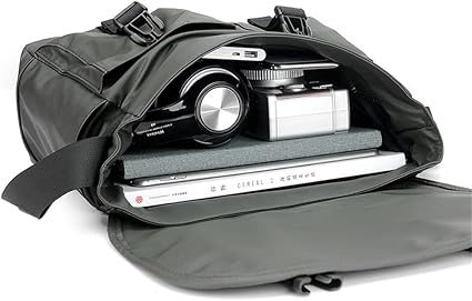 Borsa a tracolla nera aperta con fotocamera, laptop e quaderno all'interno. Ideale per viaggi, lavoro e fotografia. Accessori tecnologici organizzati.