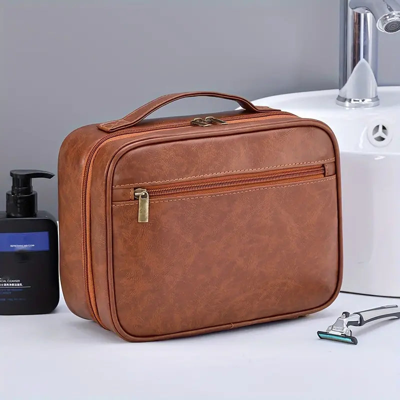 Borsa da toilette in pelle marrone con zip, posizionata su un lavandino bianco. Include dispenser sapone e rasoio. Elegante e pratica per viaggi.
