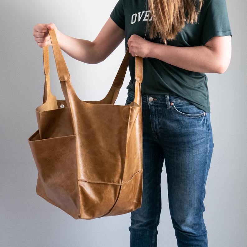 Donna con borsa shopper in pelle marrone, tasche laterali, indossa jeans e maglietta verde. Accessorio moda elegante e pratico per lo shopping.
