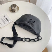 Marsupio nero in pelle su tavolo bianco, con catena decorativa e cinghia regolabile. Accessorio moda unisex, stile urbano e contemporaneo.