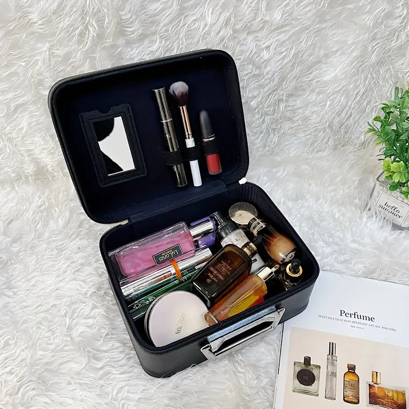 Valigetta cosmetica nera aperta su tappeto bianco, contenente profumi, rossetti, pennelli trucco e specchietto. Accanto, rivista di profumi e pianta decorativa.