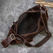 Borsa a tracolla in pelle marrone aperta, con cuciture bianche e fibbia dorata, su sfondo grigio. Accessorio moda uomo, stile vintage.