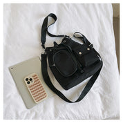 Borsa a tracolla nera su letto bianco, accanto a smartphone e tablet. Design moderno, ideale per moda urbana e accessori tecnologici.