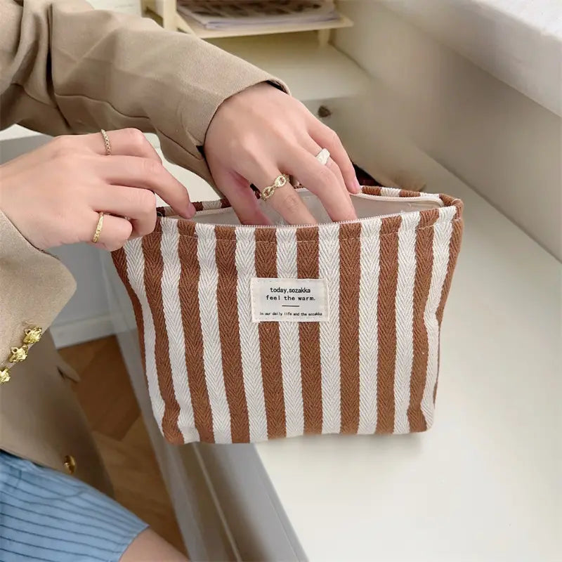 Borsa a righe marroni e bianche in tessuto, con etichetta centrale, tenuta da una persona. Accessorio moda casual, ideale per l'uso quotidiano.