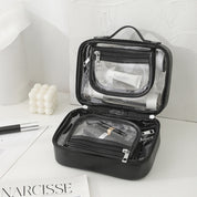 Borsa da toilette trasparente nera aperta su tavolo bianco, con scomparti multipli e prodotti cosmetici. Design elegante, ideale per viaggi e organizzazione.