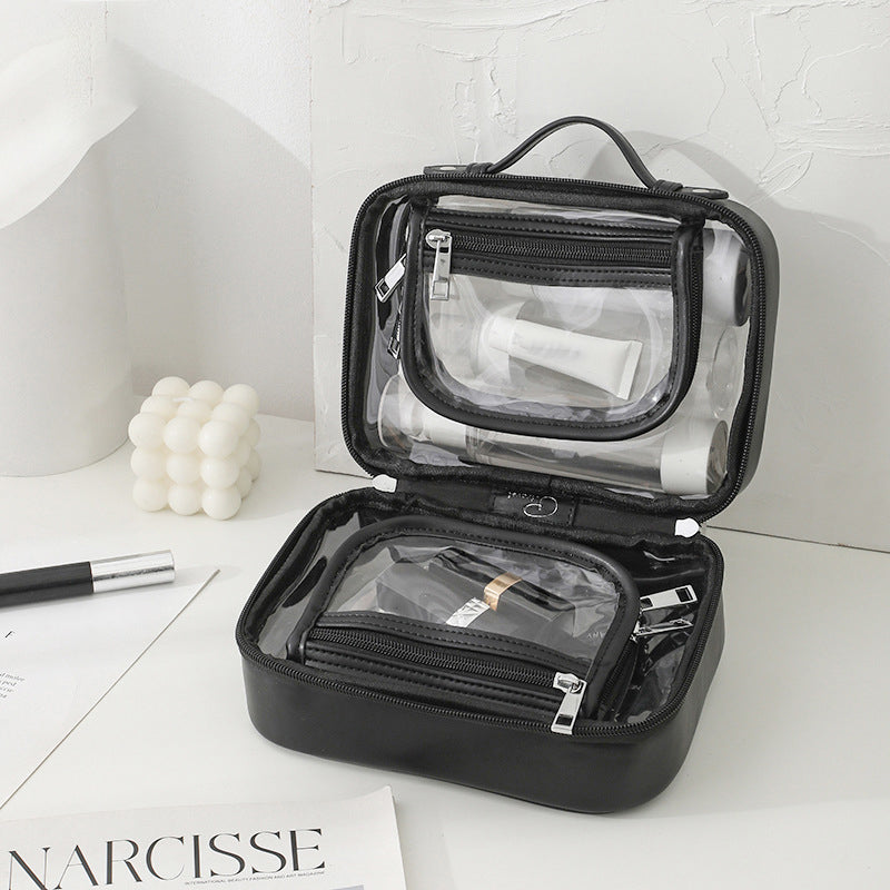 Borsa da toilette trasparente nera aperta su tavolo bianco, con scomparti multipli e prodotti cosmetici. Design elegante, ideale per viaggi e organizzazione.