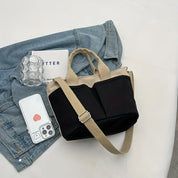 Borsa a tracolla nera e beige su giacca di jeans, con smartphone, bicchiere e libro. Accessori moda donna, stile casual chic.