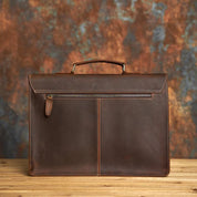Elegante valigetta in pelle marrone su sfondo sfocato, ideale per lavoro e ufficio. Design classico con manico robusto e cuciture a vista.