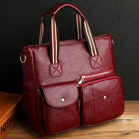 Borsa a mano in pelle rossa con tasche frontali, manici a righe, design elegante. Accessorio moda donna, ideale per lavoro e tempo libero.