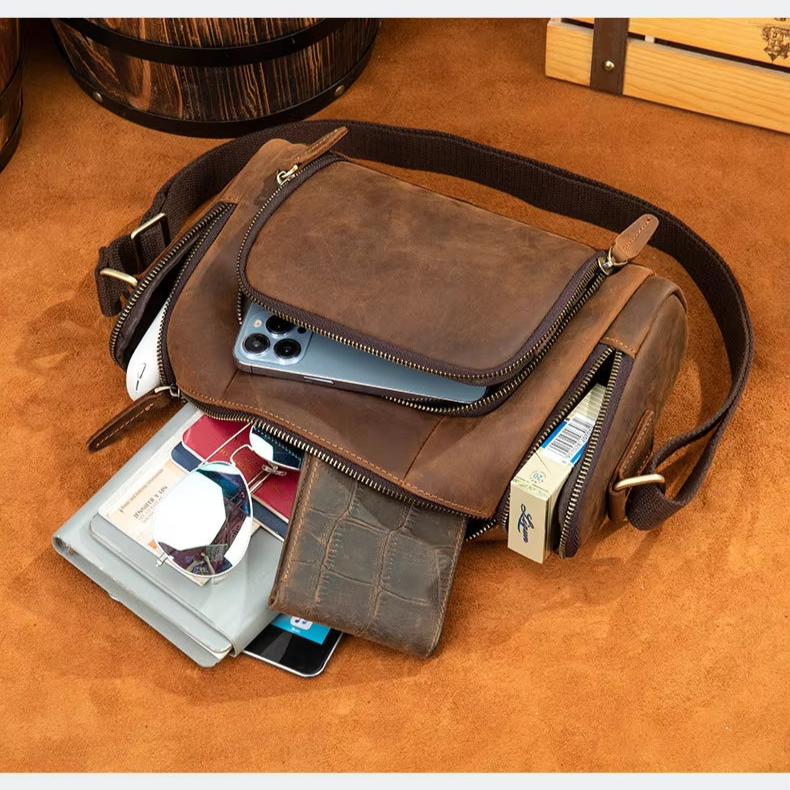 Borsa a tracolla in pelle marrone con smartphone, portafoglio, occhiali e pacchetto di sigarette. Accessori moda uomo, stile vintage.