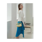 Donna con abito blu asimmetrico e giacca bianca, borsa a tracolla gialla, in un ambiente moderno. Moda elegante, abbigliamento femminile contemporaneo.
