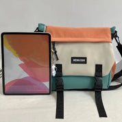 Borsa a tracolla multicolore con chiusura a fibbia, accanto a un tablet. Design moderno, ideale per viaggi e uso quotidiano.