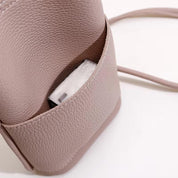 Borsa a tracolla in pelle rosa con texture, tasca esterna contenente un pacchetto di fazzoletti. Accessorio moda elegante e pratico.