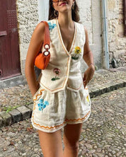 Donna con completo estivo bianco ricamato a fiori, borsa arancione, orecchini a cerchio, su strada acciottolata. Moda estiva, abbigliamento casual.