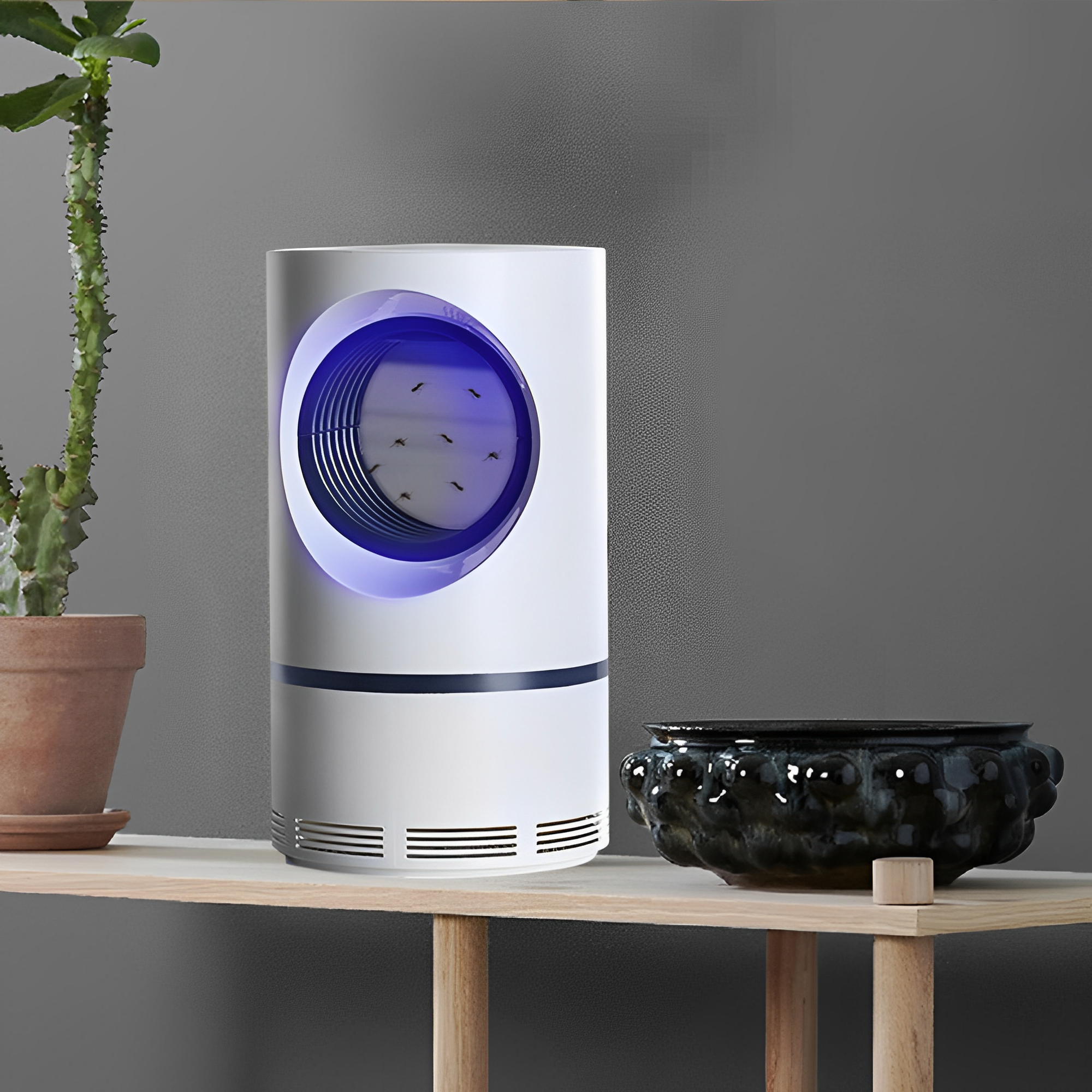 Trappola per zanzare elettrica bianca su mensola di legno, con luce LED blu, accanto a pianta in vaso e ciotola nera decorativa.