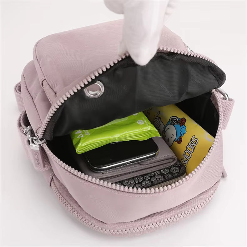 Zaino compatto rosa aperto, mostra tasca interna con smartphone, fazzoletti e snack. Design pratico, ideale per viaggi e uso quotidiano.