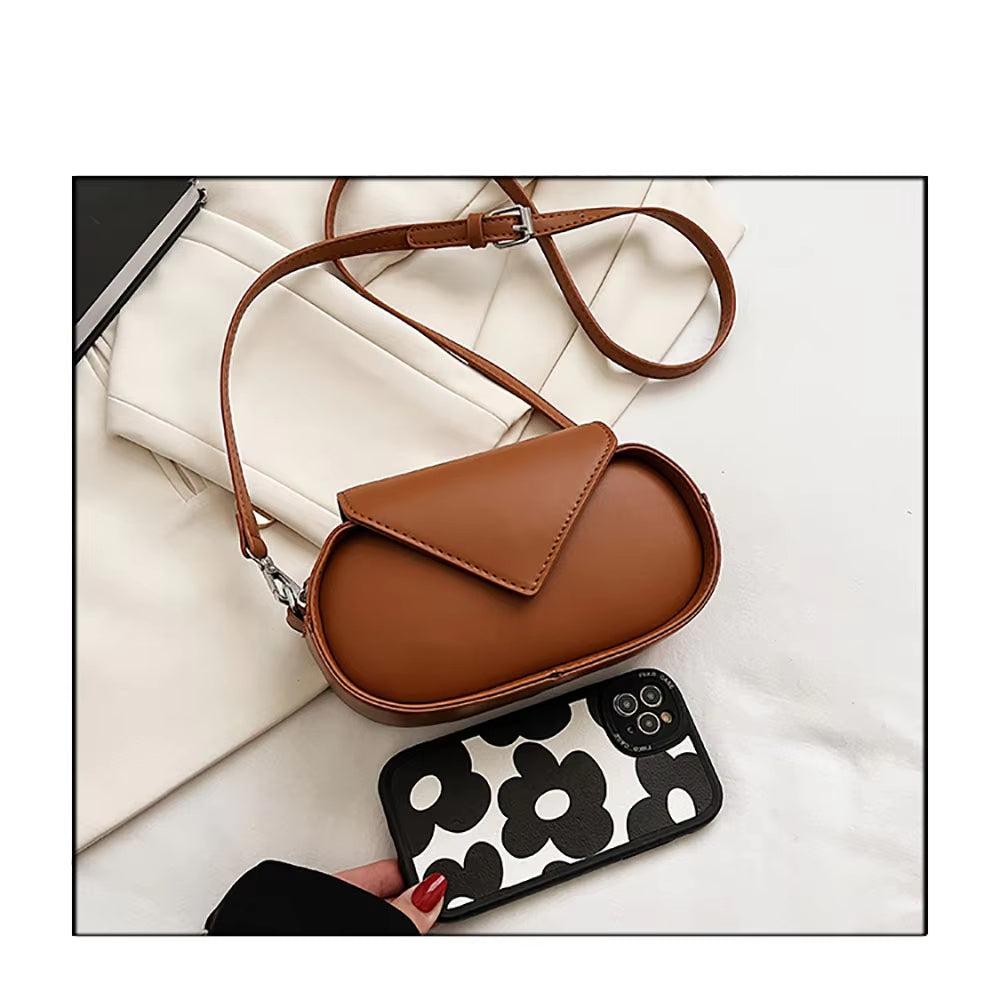 Borsa a tracolla in pelle marrone su sfondo bianco, accanto a smartphone con cover floreale. Accessorio moda elegante e versatile per donna.