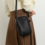 Borsa a tracolla in pelle nera, elegante e compatta, indossata su abito marrone. Accessorio moda donna, ideale per look casual e formali.