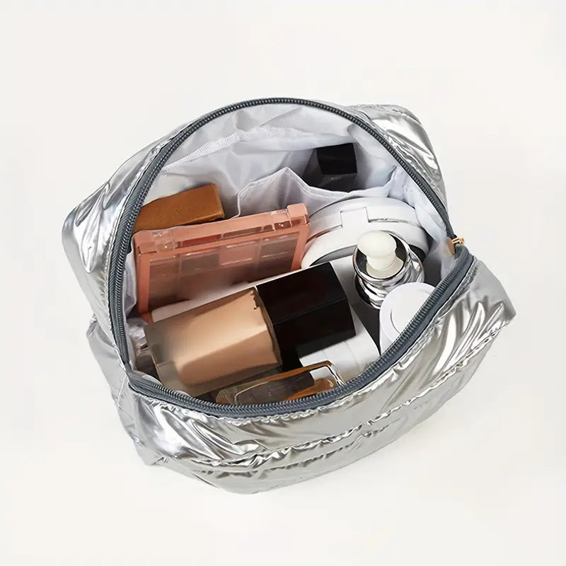 Borsa cosmetica argento aperta con trucchi: fondotinta, palette ombretti, flaconi skincare. Accessori bellezza, organizzazione trucco viaggio.