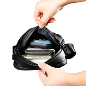 Mani che aprono una borsa a tracolla nera, mostrando smartphone, portafoglio e chiavi all'interno. Accessorio moda uomo, pratico e spazioso.