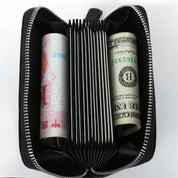 Portafoglio nero aperto con cerniera, contenente banconote di yuan e dollari USA. Design compatto, ideale per viaggi e organizzazione denaro.