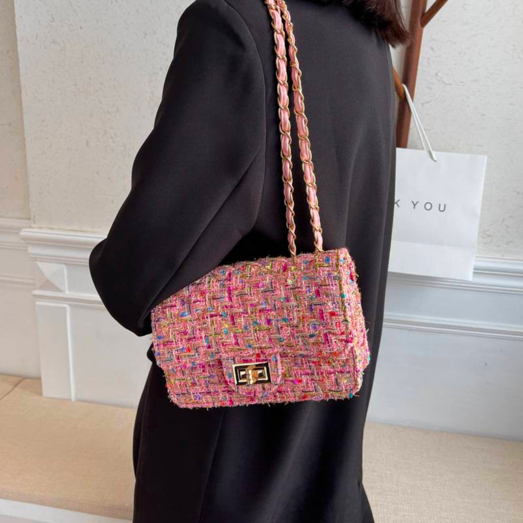 Borsa a tracolla in tweed multicolore, chiusura a scatto, indossata da donna in abito nero. Accessorio moda elegante e trendy.