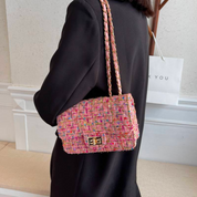 Borsa a tracolla in tweed multicolore, chiusura a scatto, indossata da donna in abito nero. Accessorio moda elegante e trendy.