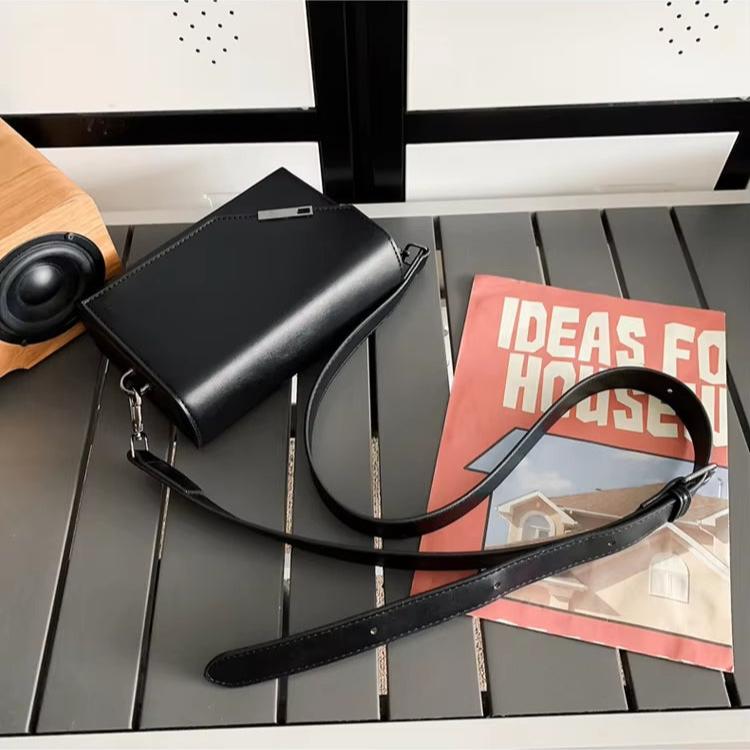 Borsa a tracolla nera elegante su tavolo grigio, accanto a rivista di design per la casa. Accessorio moda donna, stile minimalista.