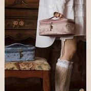 Donna con calze di pizzo bianco tiene una borsa cosmetica rosa, accanto a una borsa blu su sedia vintage. Elegante, retrò, accessori moda.